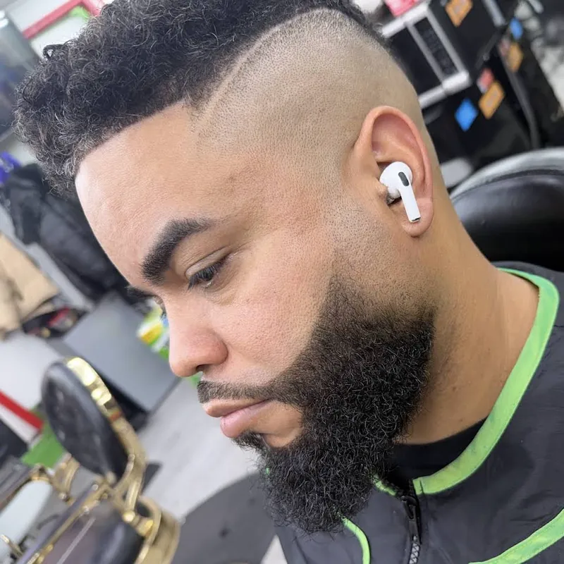 Fade alto con rizos arriba, line-up definido y barba completa