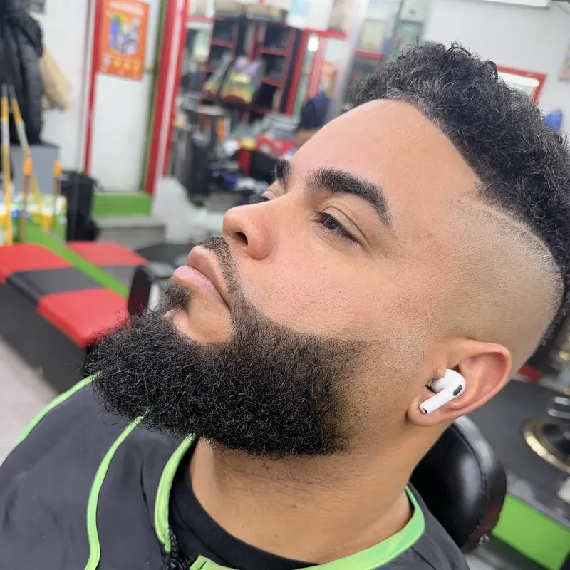 Corte con navaja: fade alto con raya marcada, rizos arriba y barba completa